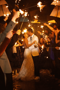 Nighttime wedding exit with bride and groom kissing surrounded by sparklers