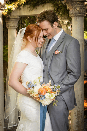 Joyful bride and groom smiling together outdoors holding a vibrant summer wedding bouquet