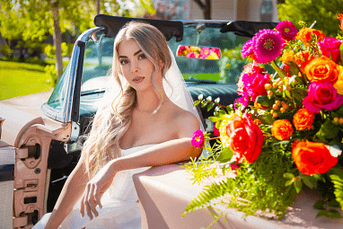 Bride in a classic lace gown sitting in a vintage car during an outdoor wedding session