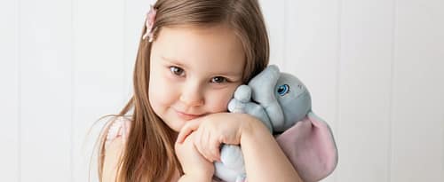 child Children's portrait photography in Ogden Utah featuring a young girl hugging a soft elephant plush toy with natural window lighting.